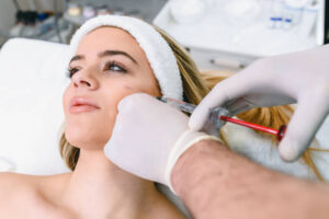 The doctor cosmetologist makes the Rejuvenating facial injections procedure for tightening and smoothing wrinkles on the face skin of a beautiful, young woman in a beauty salon. Hands of cosmetologist are close-ups that inject hyaluronic acid into the cheekbone area of the woman.